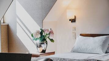 A hotel room with a bed, a bedside table with a vase of flowers, a lamp, and a view of the outside.