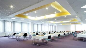 A conference room with rows of tables and chairs, large windows, and a modern ceiling design.