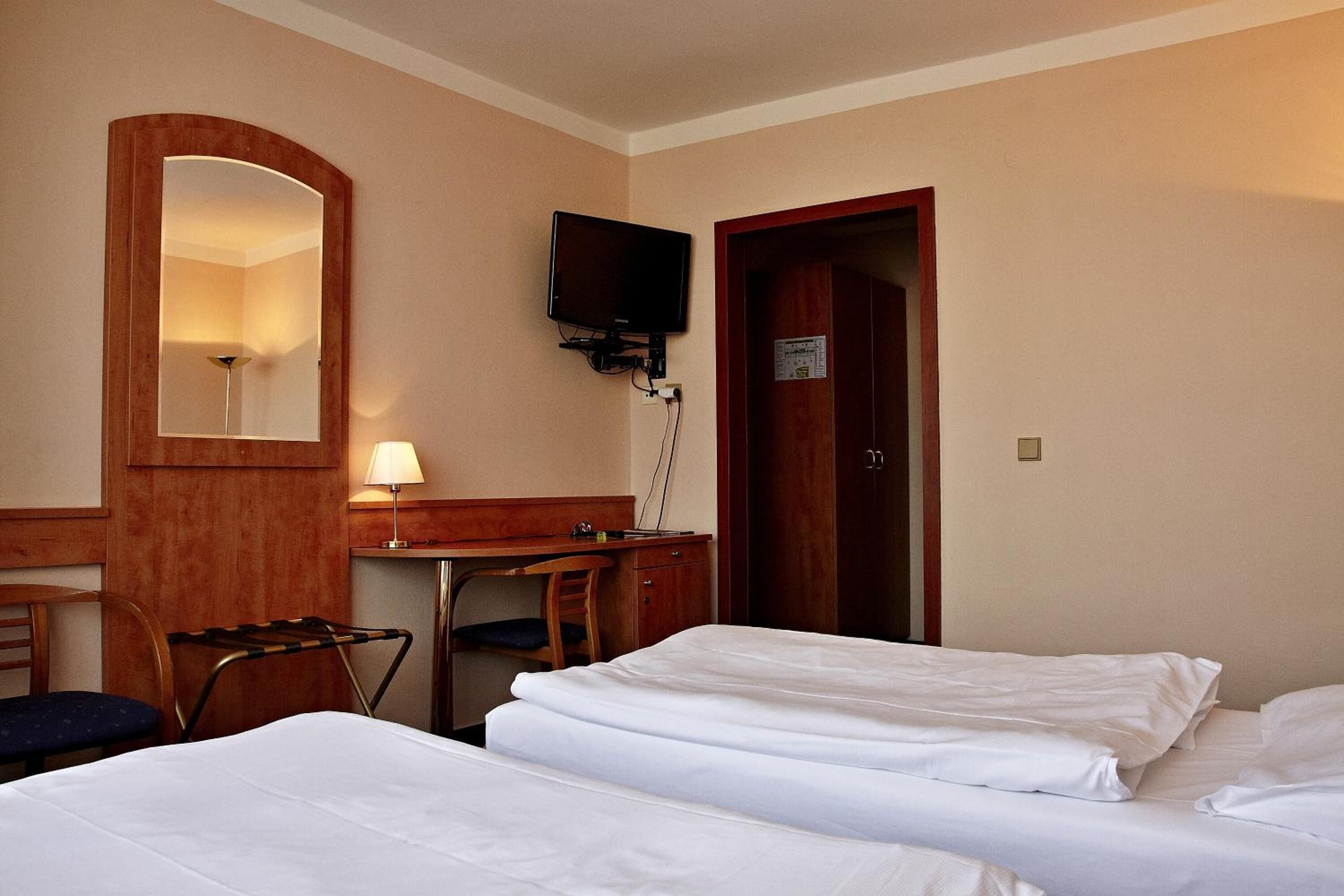 A hotel room with two beds, a desk with a chair, a television mounted on the wall, and a door.
