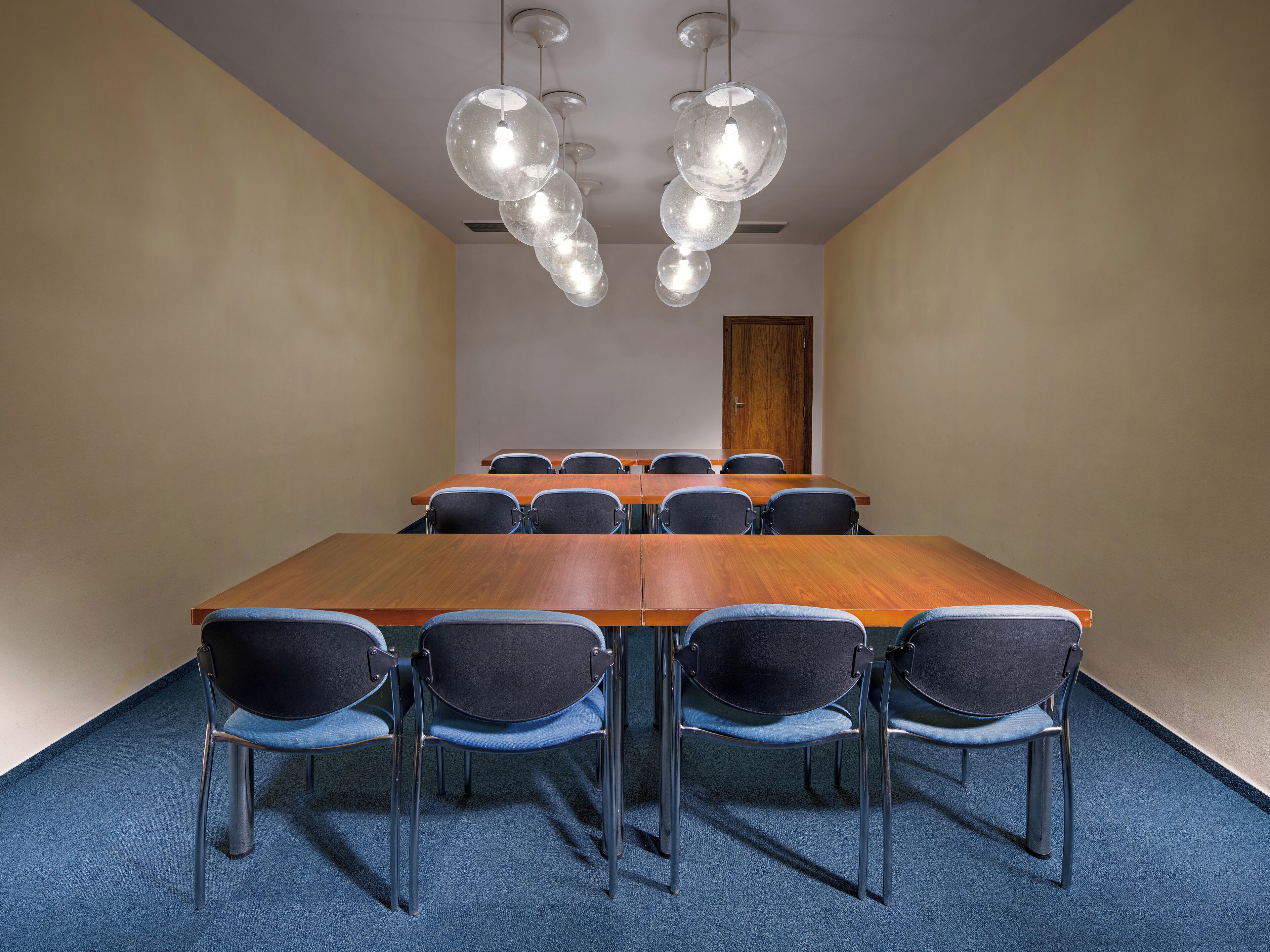 A conference room with a long wooden table, black chairs, and hanging spherical light fixtures.