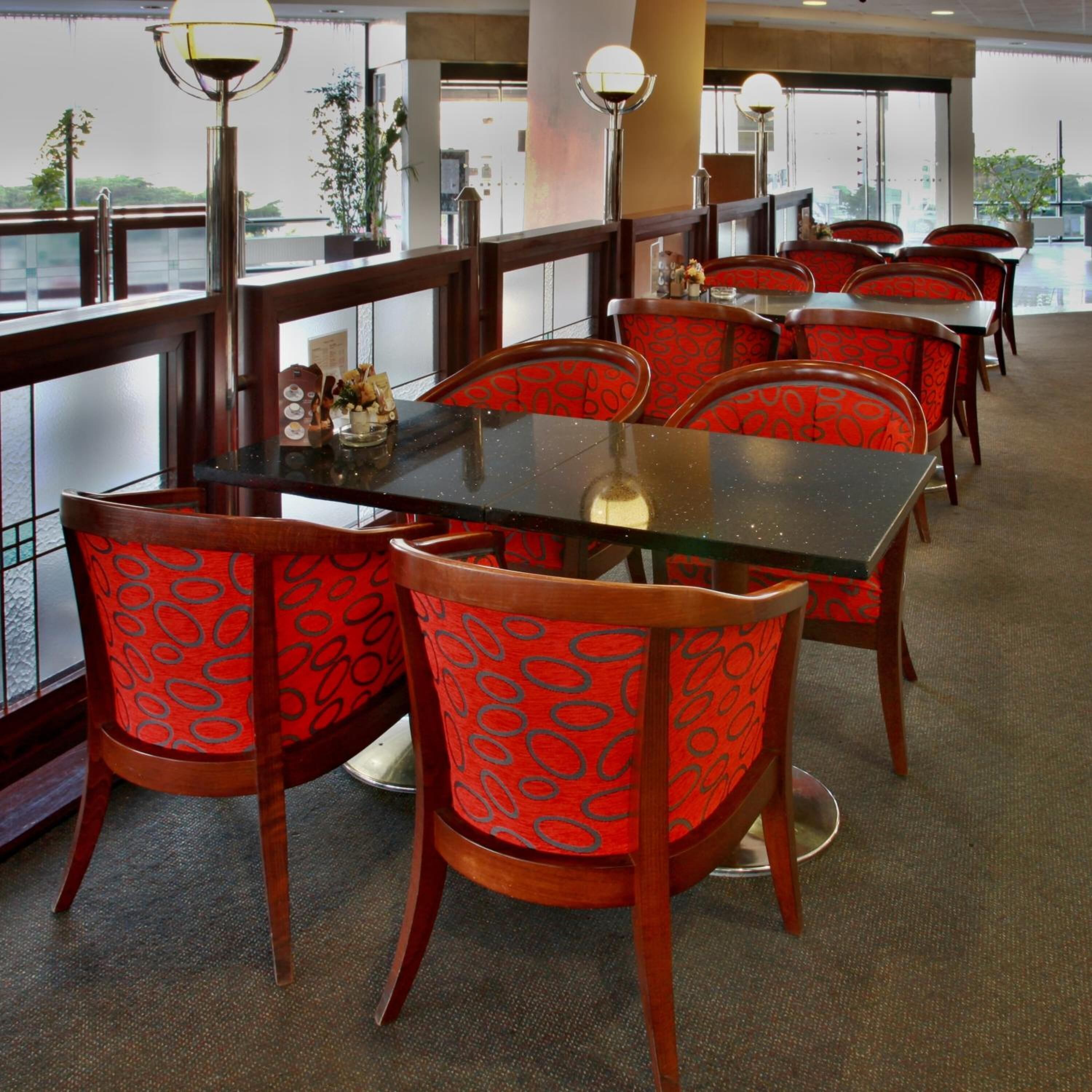 A restaurant with a glass railing, red patterned chairs, and a view of the outside.