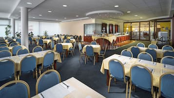 A large conference room with multiple tables and chairs, a buffet area, and a reception desk.