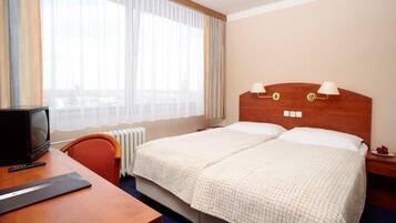 Een hotelkamer met een bed, een bureau met een computer, een stoel en een raam met gordijnen.