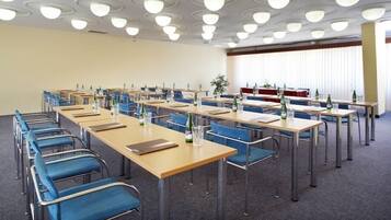 Une salle de conférence avec des rangées de tables et de chaises, équipée de bouteilles d’eau et de verres.