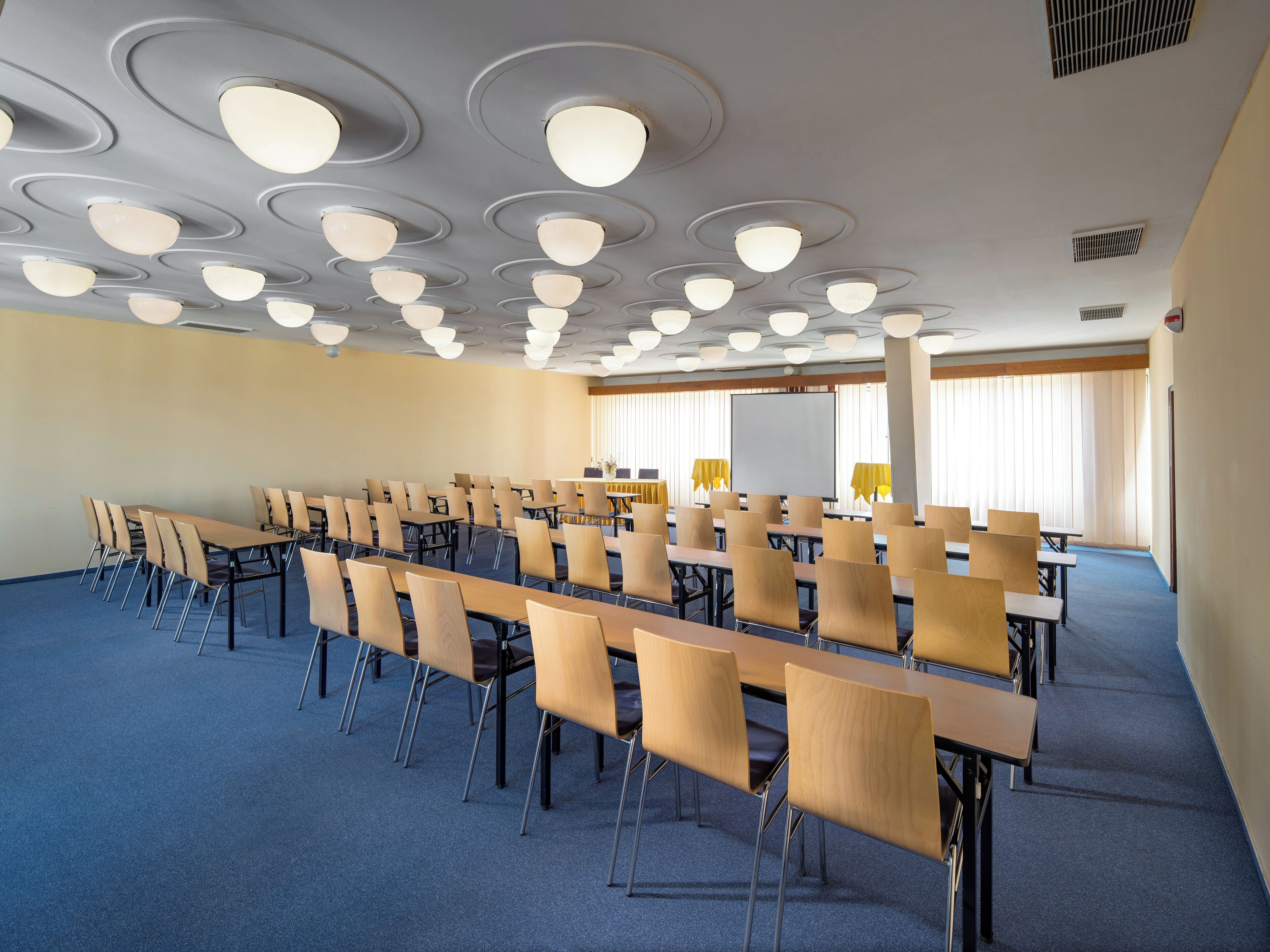 A conference room with rows of tables and chairs, a whiteboard, and a projector screen.