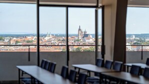 Un salón de conferencias con mesas y sillas, amplias ventanas que ofrecen vistas de un paisaje urbano con edificios históricos.