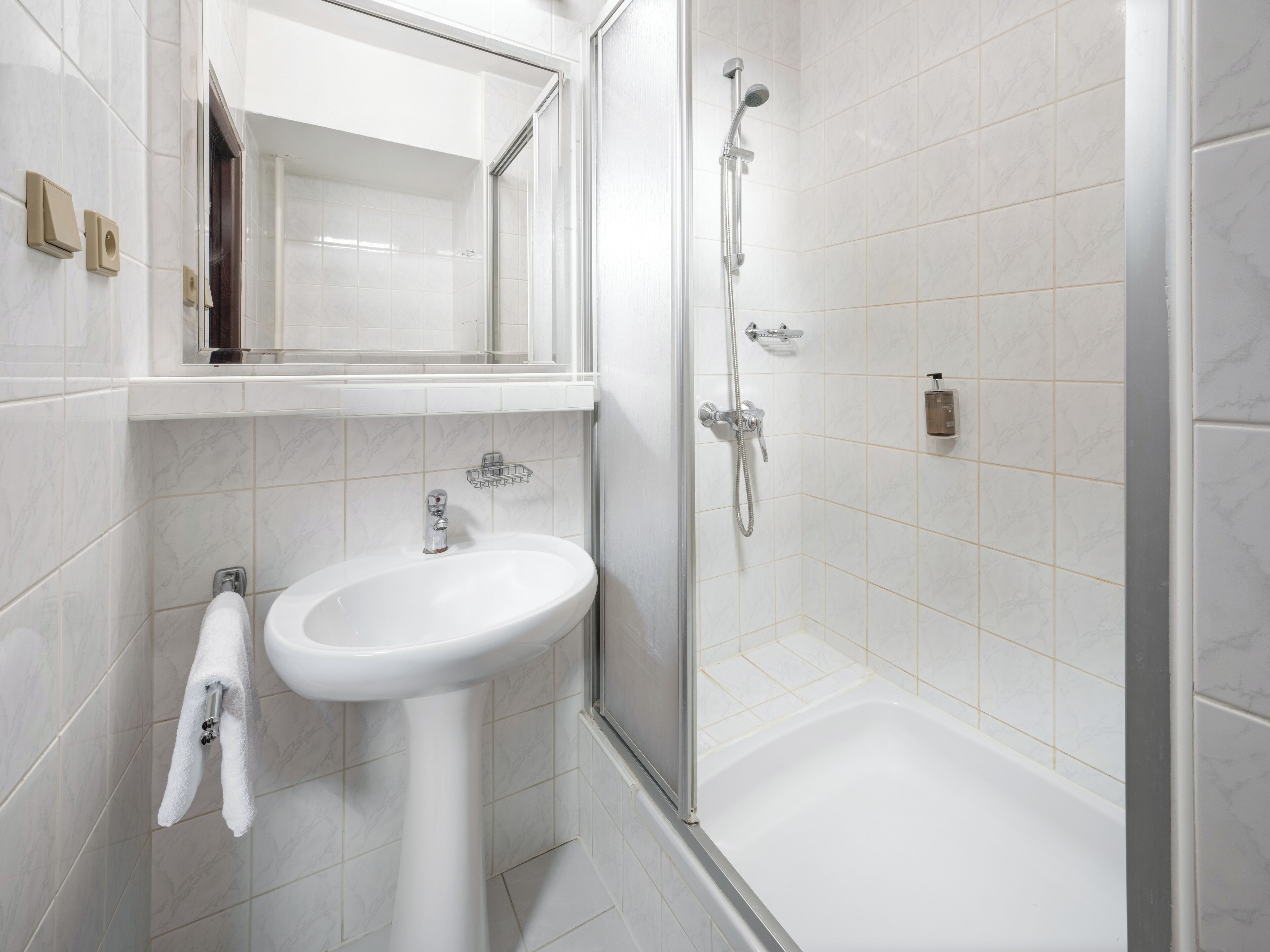 Un baño moderno con lavamanos, espejo y ducha blancos.