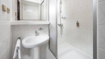 Un baño moderno con lavamanos, espejo y ducha blancos.