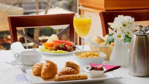 A breakfast table with croissants, fruit, a glass of orange juice, and a coffee pot.