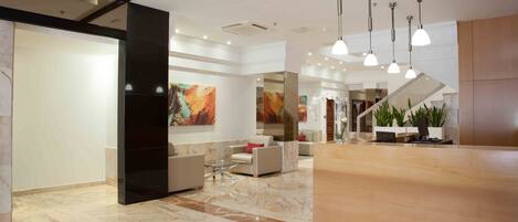 A modern lobby with marble flooring, a reception desk, seating area, and artwork on the walls.