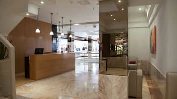 A modern hotel lobby with a marble floor, a reception desk, and a seating area.