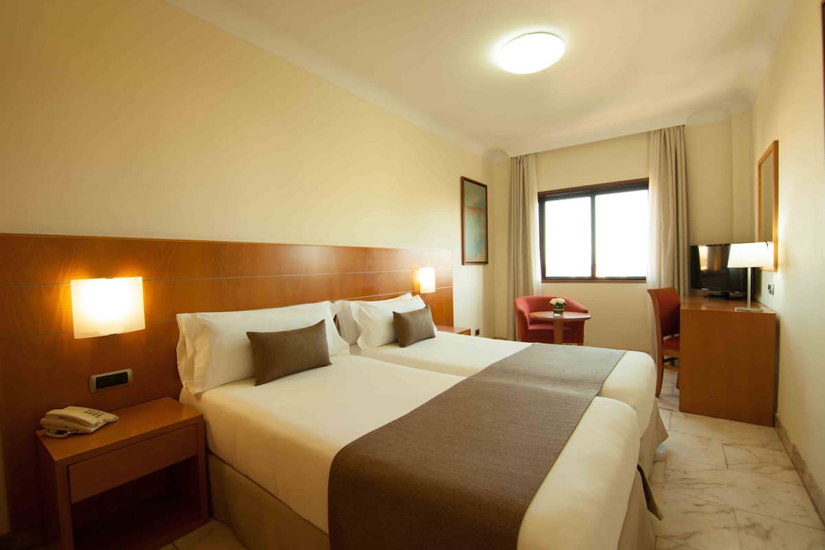 A hotel room with two beds, a nightstand with a phone, a desk with a chair, and a television.