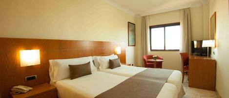 A hotel room with two beds, a nightstand with a phone, a desk with a chair, and a television.