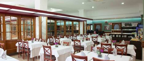 Un restaurante con varias mesas y sillas, una zona de bufé y una cocina al fondo.