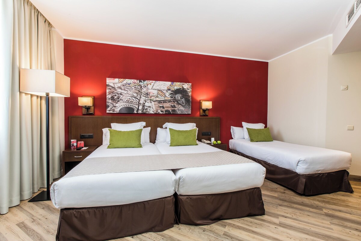 A hotel room with two beds, a large painting on the wall, and a nightstand with a lamp.