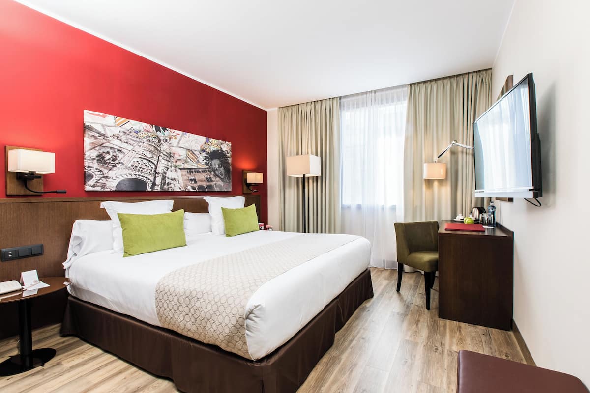 Una camera d'albergo con un letto grande, due comodini, una scrivania, una sedia e una TV.