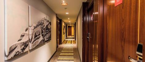 Pasillo de hotel con una puerta de madera con la etiqueta "707", alfombra a rayas y un muro con una gran obra de arte abstracta.
