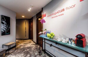 A hotel lobby with a glass table displaying a coffee machine, cups, and a vase with flowers. A sign reads "Advantage CLUB floor Leonardo Hotels." - Leonardo Hotel Barcelona Gran Via (Barcelona)