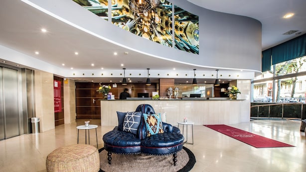 Um lobby moderno com teto curvo, área de estar com sofá e apoio para os pés estofados, área de bar e uma grande janela com vista para a rua.
