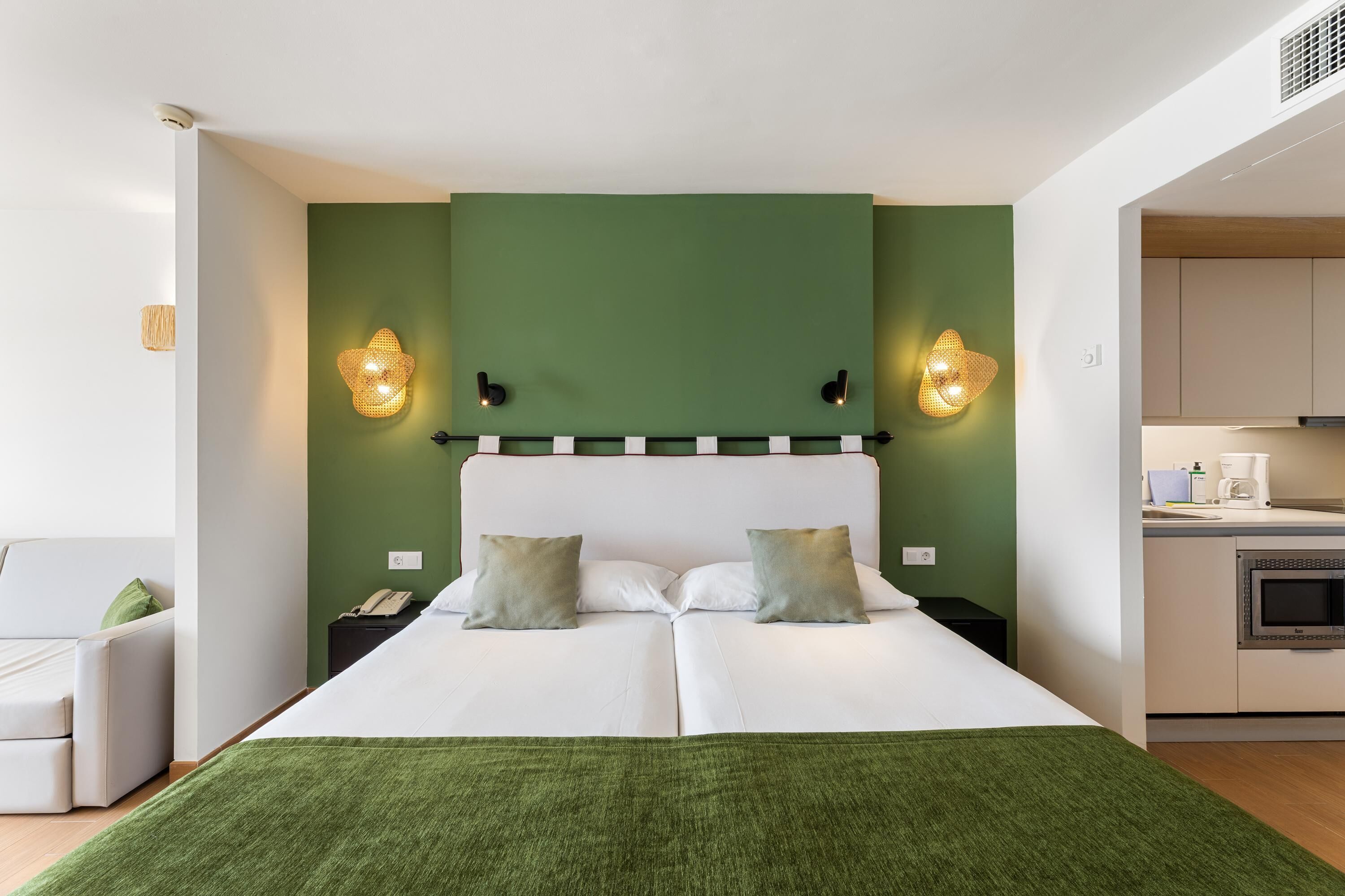A hotel room with a bed, bedside tables, a green accent wall, and a kitchenette.