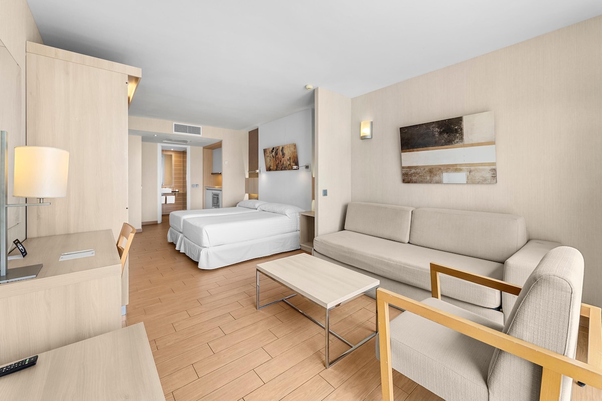 Ett modernt hotellrum med trägolv, en soffa, en säng, ett skrivbord och en lampa.