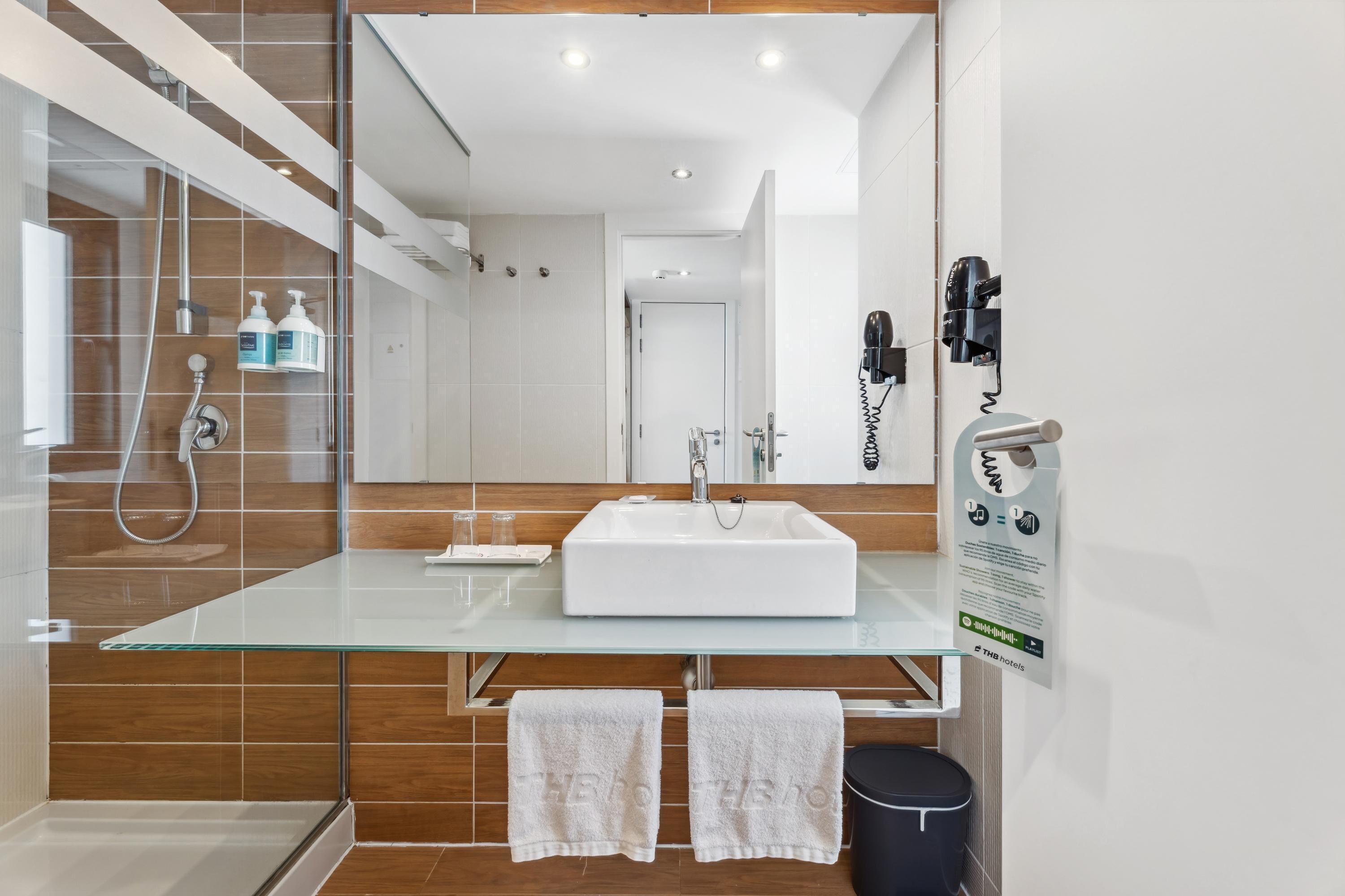 A modern bathroom with a glass vanity, a white sink, and a shower area.