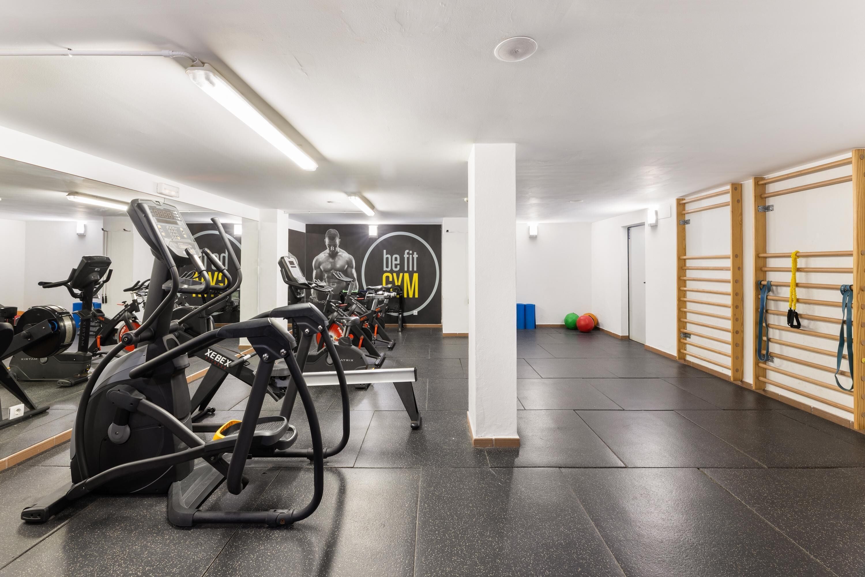 A gym with treadmills, a mirrored wall, and a 'be fit gym' sign.