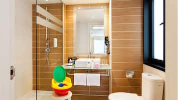 A modern bathroom with a glass shower enclosure, a toilet, a sink with a mirror above, and a window.