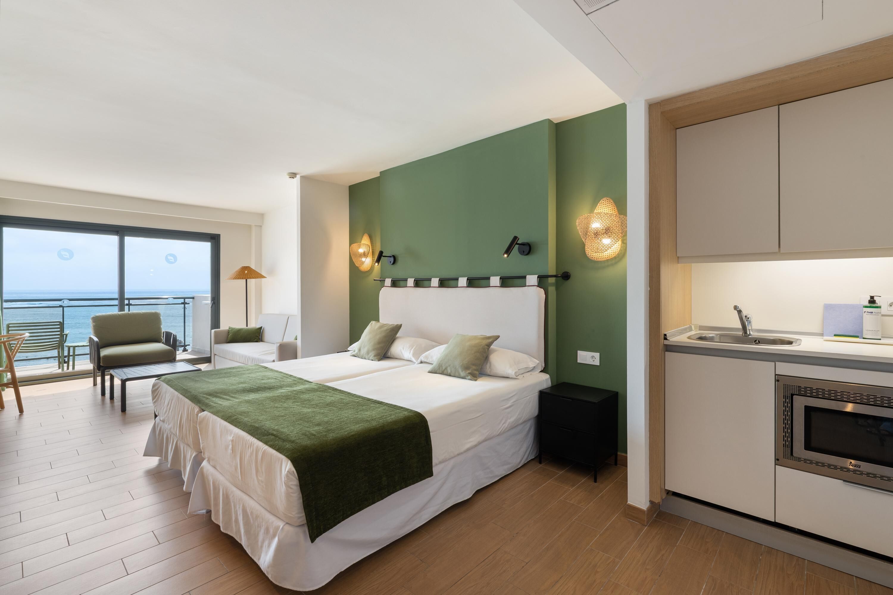 Un dormitorio con cama, mesita de noche, lámpara, vista al mar y kitchenette.