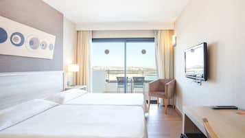 A hotel room with two beds, a desk, a chair, a TV, and a balcony with a view.