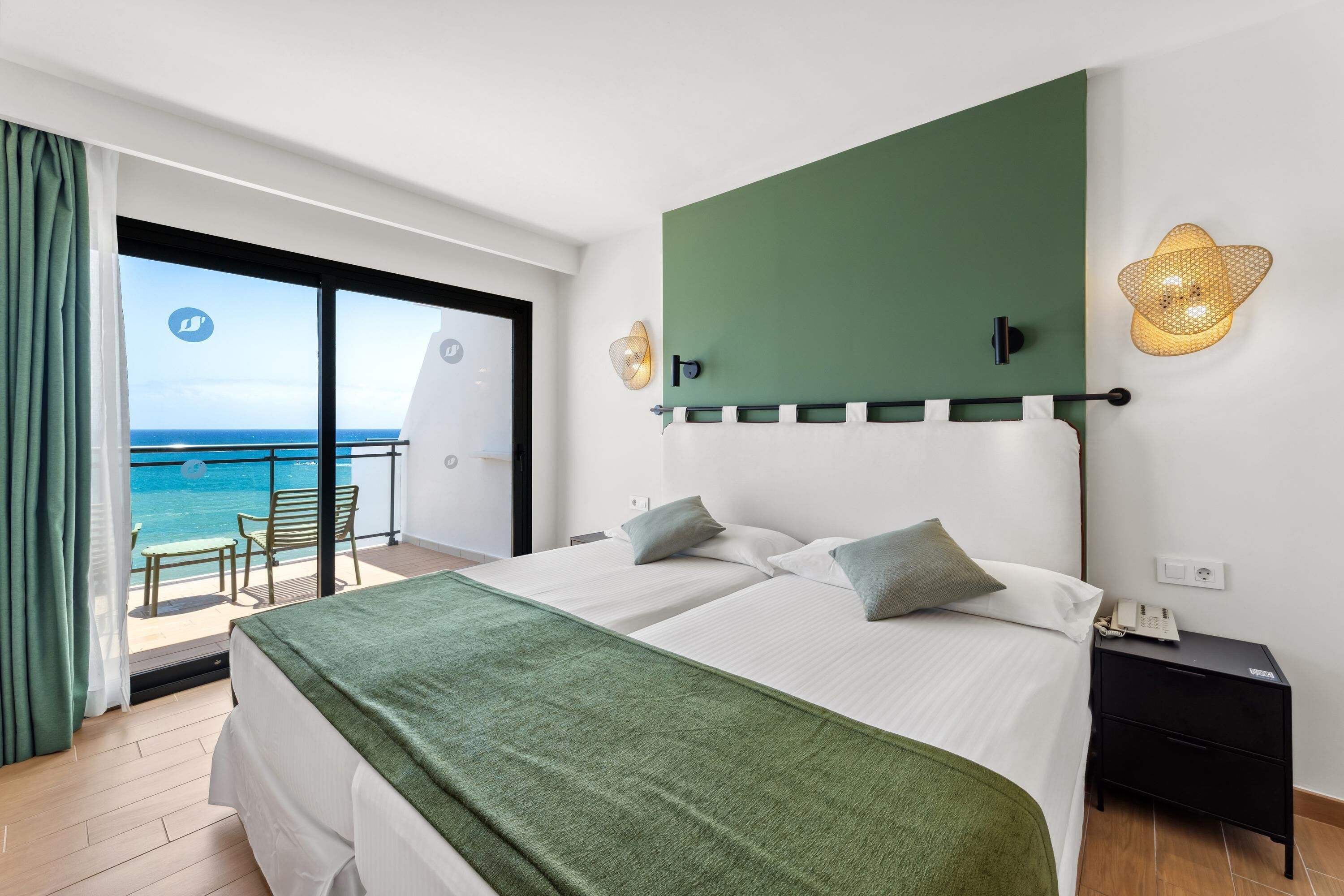 A hotel room with a bed, a nightstand, a lamp, and a view of the ocean.