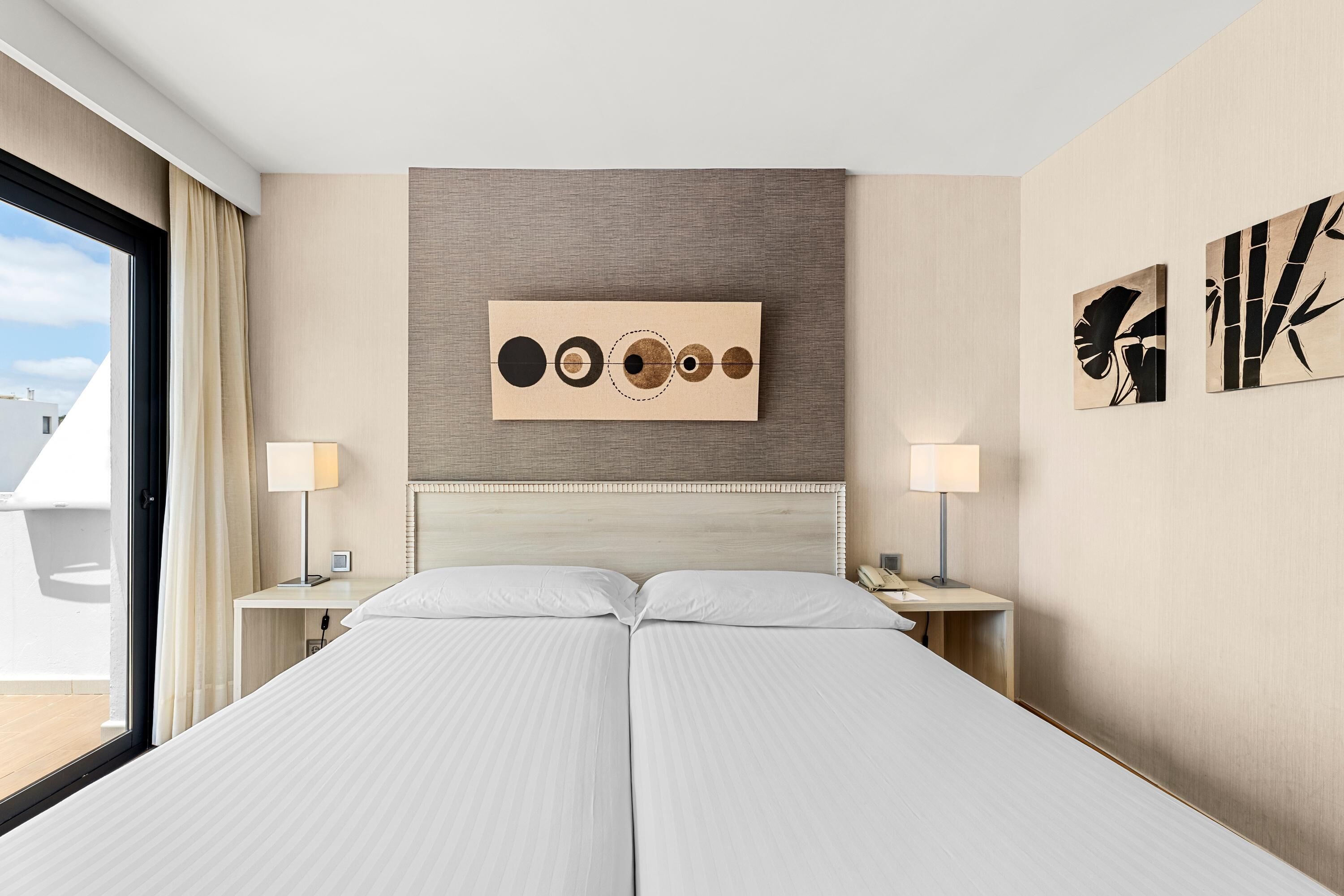 Una habitación de hotel con una cama grande, dos mesitas de noche, un cabecero y obras de arte en las paredes.