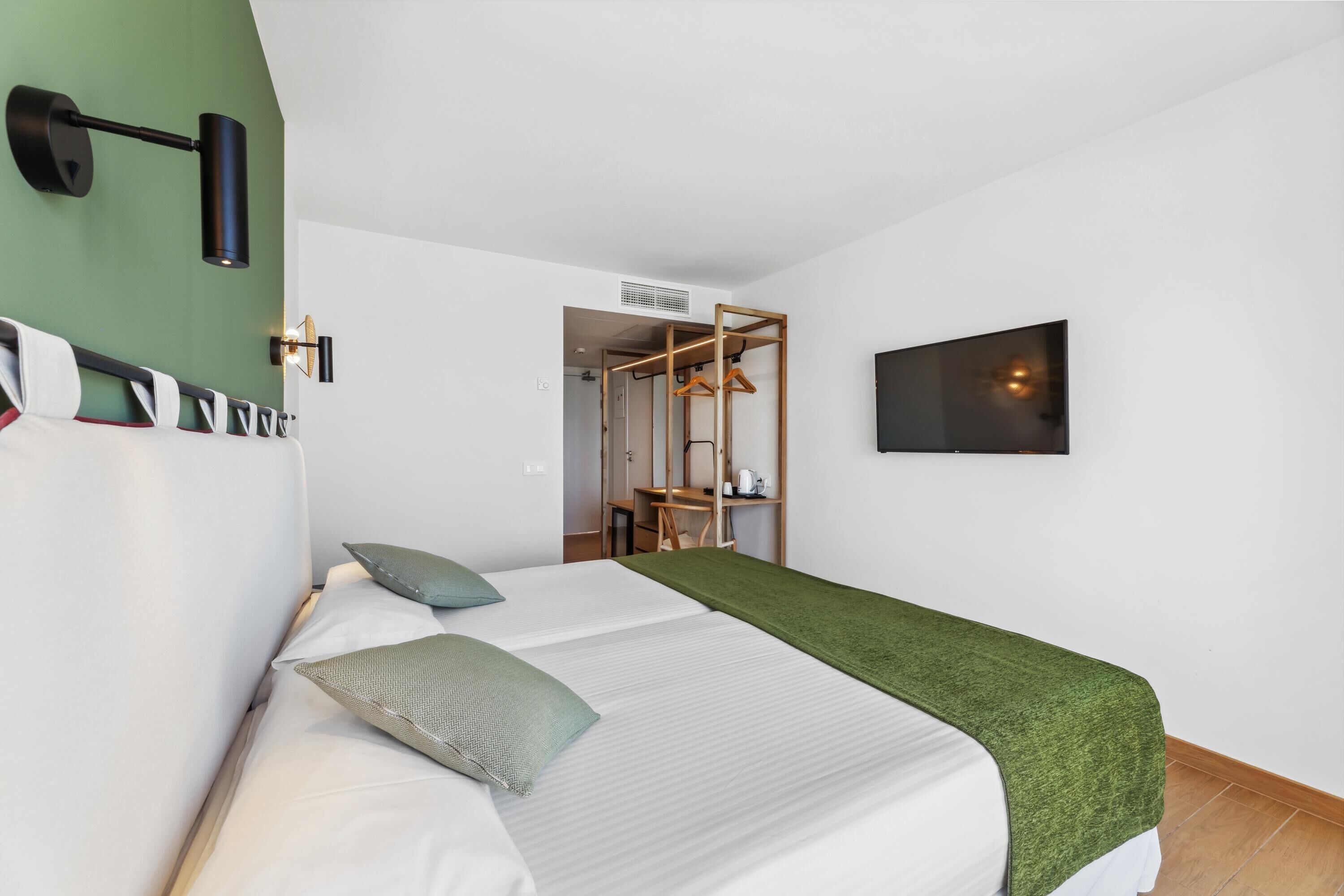 Habitación de hotel con una cama, pared verde, lámpara negra de pared y un armario de madera.