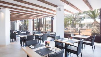 A spacious outdoor dining area with wooden beams, black wicker chairs, and tables set for two.