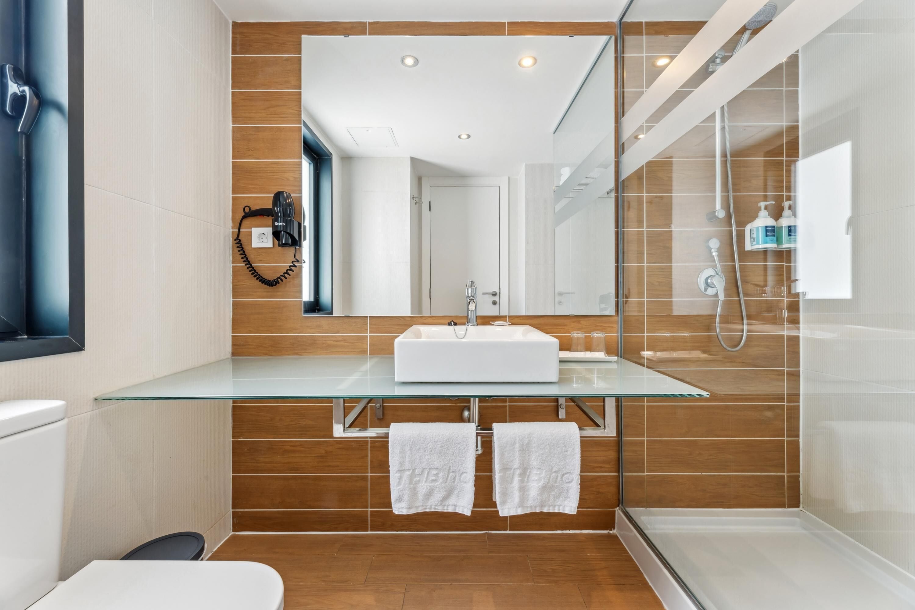 A modern bathroom with a glass vanity, a large mirror, and a shower area.