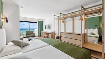 A hotel room with two beds, a desk, a chair, a wardrobe, and a balcony with a view of the sea.