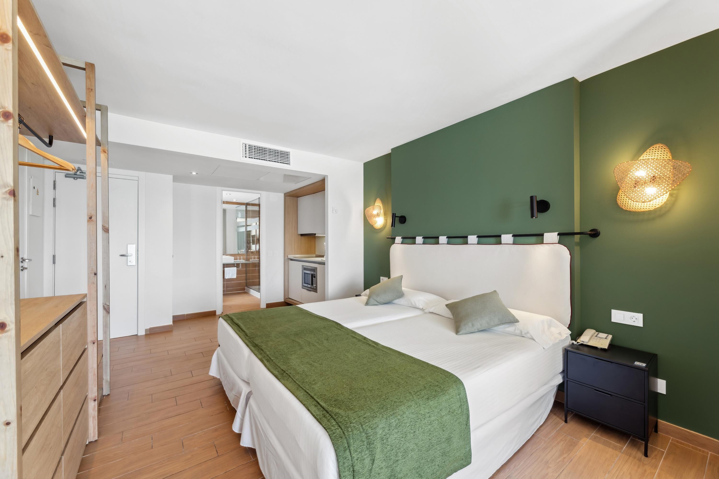 Un dormitorio con cama, mesita de noche y pared verde con lámpara.