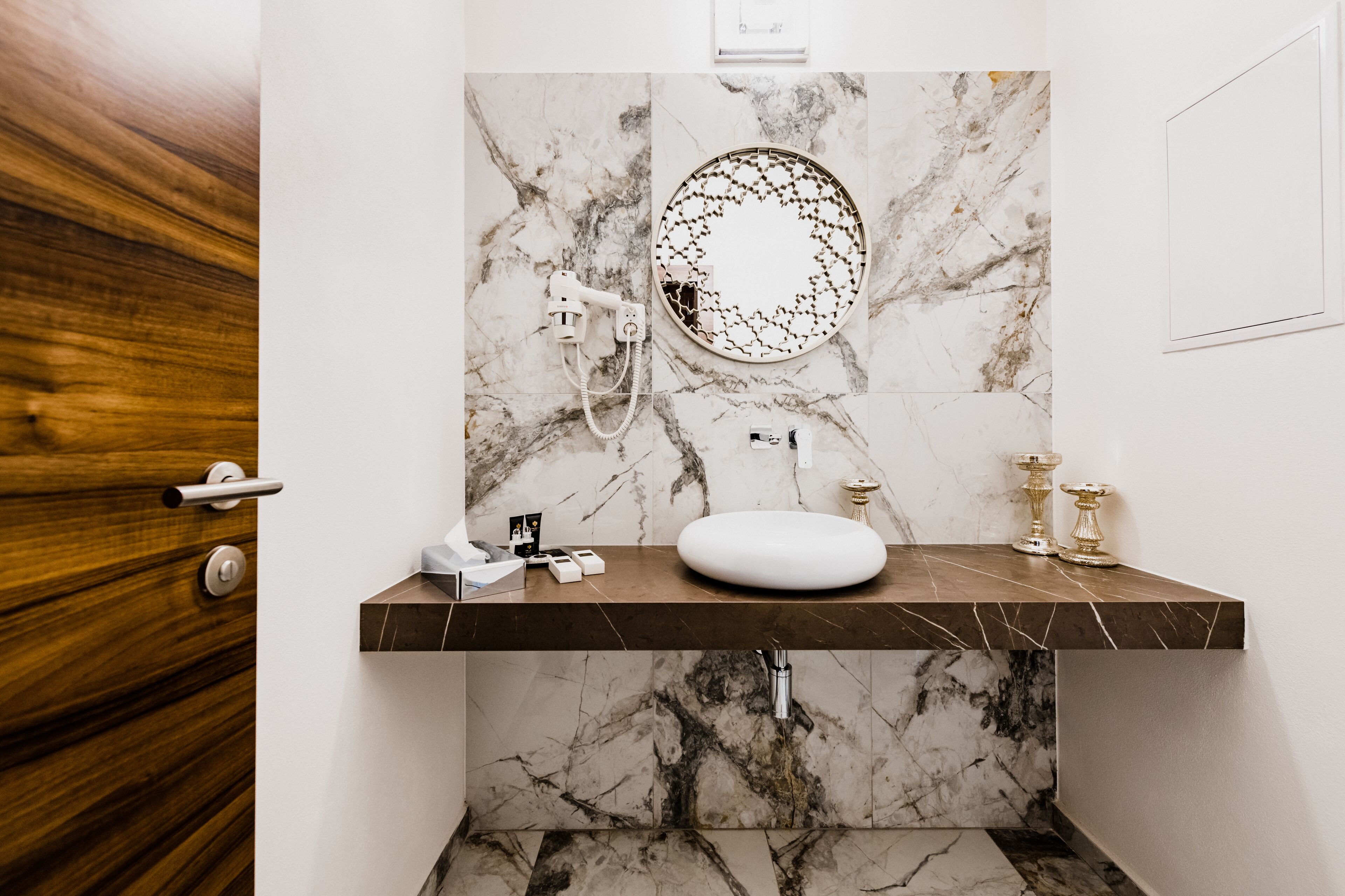 A modern bathroom with a marble sink, a round mirror, and a shower head.