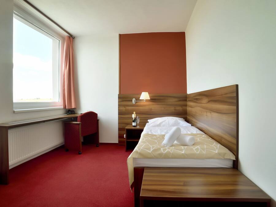 A hotel room with a bed, a desk, a chair, a nightstand, and a lamp.