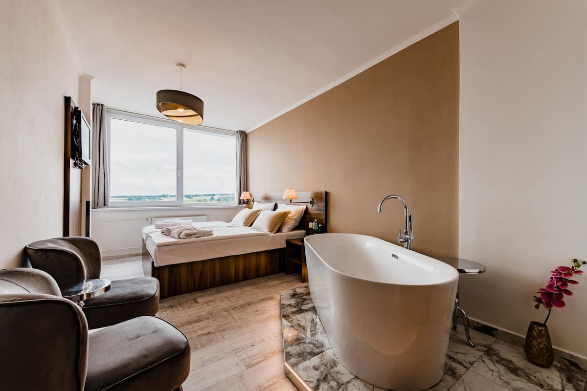 Een moderne badkamer met een vrijstaand bad, een groot raam en een zithoek met stoelen.