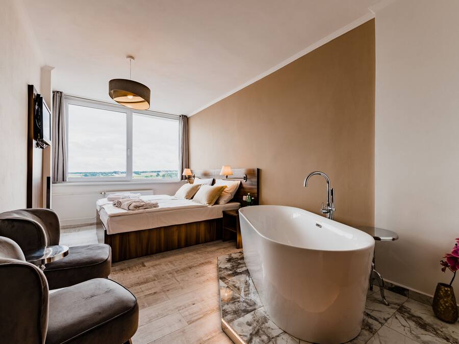 A modern bathroom with a freestanding bathtub, a large window, and a seating area with chairs.