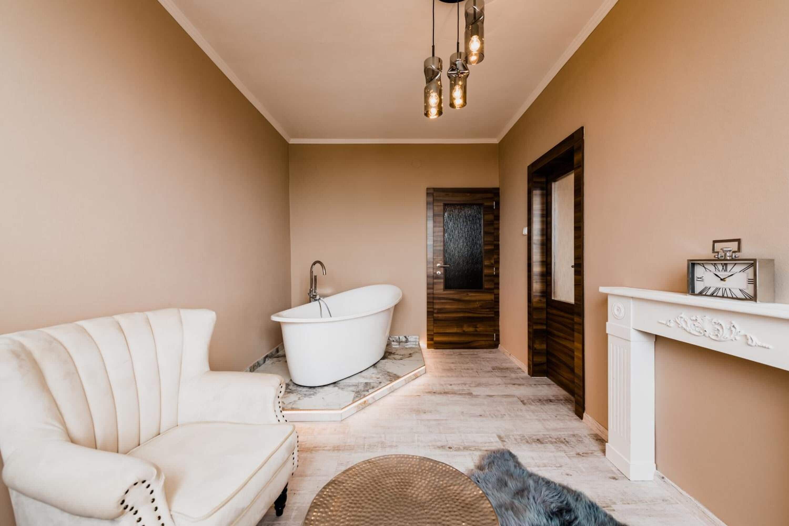 A bathroom with a white bathtub, a white chair, a wooden door, and a white fireplace.