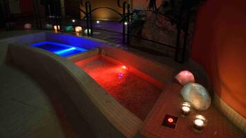 Un área de spa con dos jacuzzis, uno con iluminación azul y otro con iluminación roja, rodeados de velas y rocas decorativas.