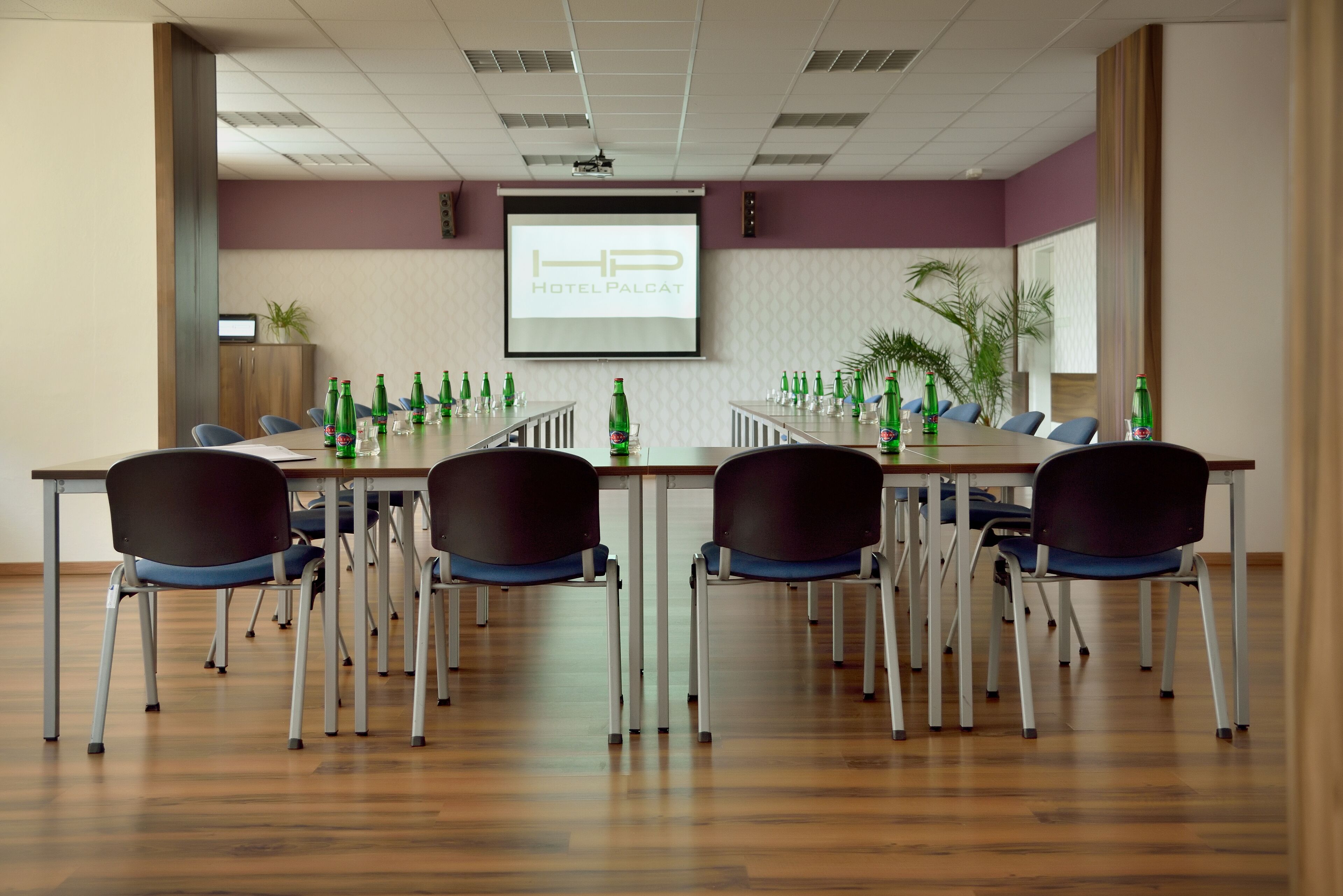 Un salón de conferencias con una larga mesa, varias sillas y una pantalla de proyector mostrando 