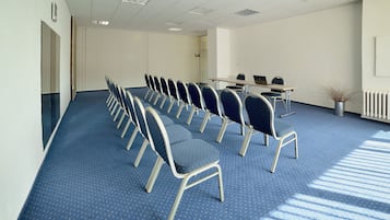 Un salón de conferencias con filas de sillas, una mesa con portátiles y un radiador.