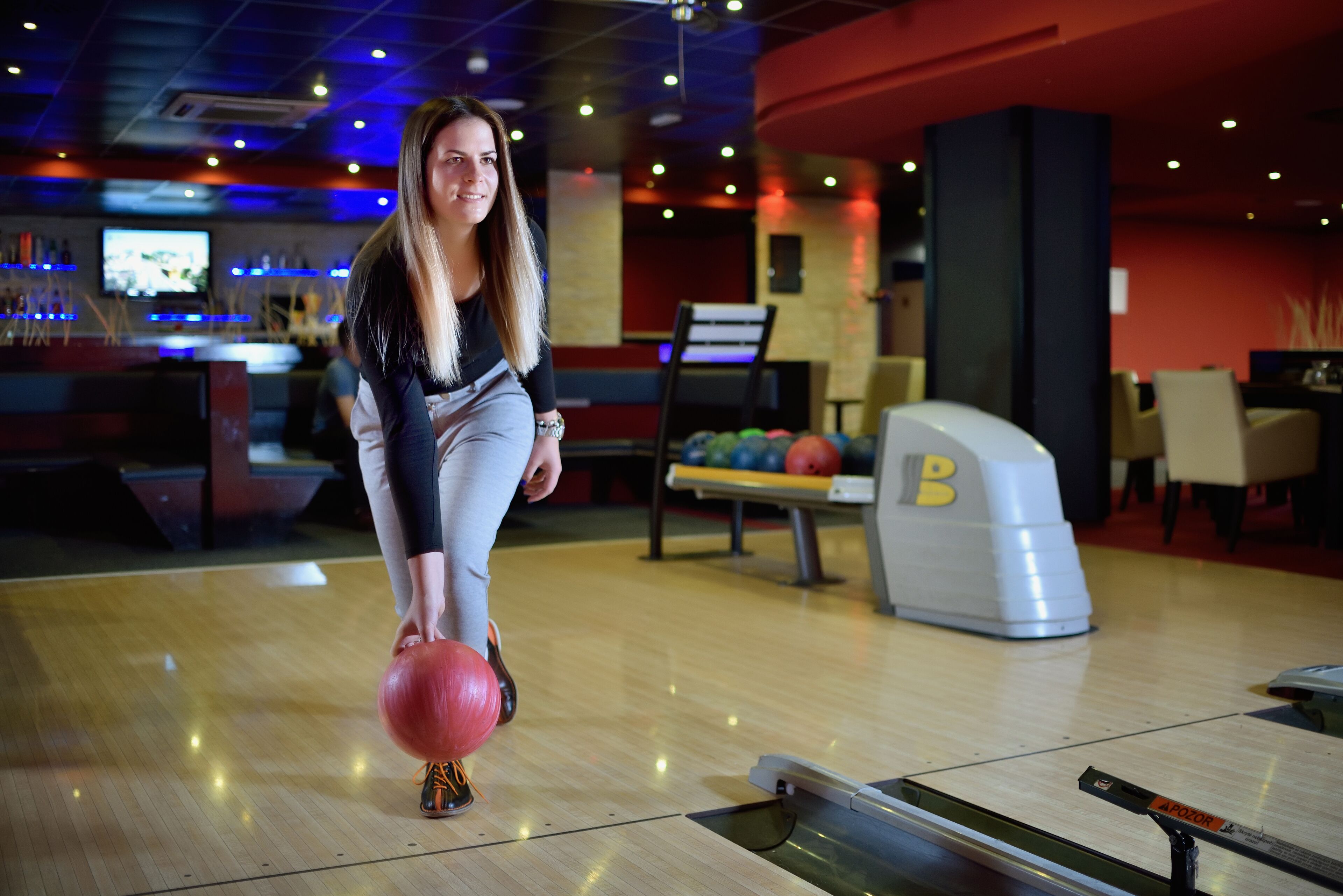 A bowling alley with a bowling ball in motion, a bowling lane, and a pinsetter in the background.