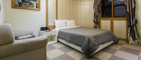 A neatly arranged bedroom with a bed, a chair, a nightstand, and a wall-mounted picture.