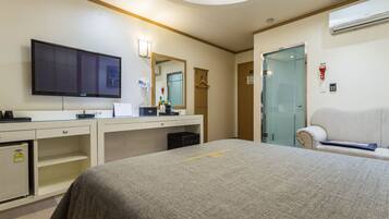 Una habitación de hotel con cama, televisor, escritorio, espejo y sofá.