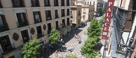 Un patio con suelo a cuadros, rodeado de edificios con balcones y árboles.