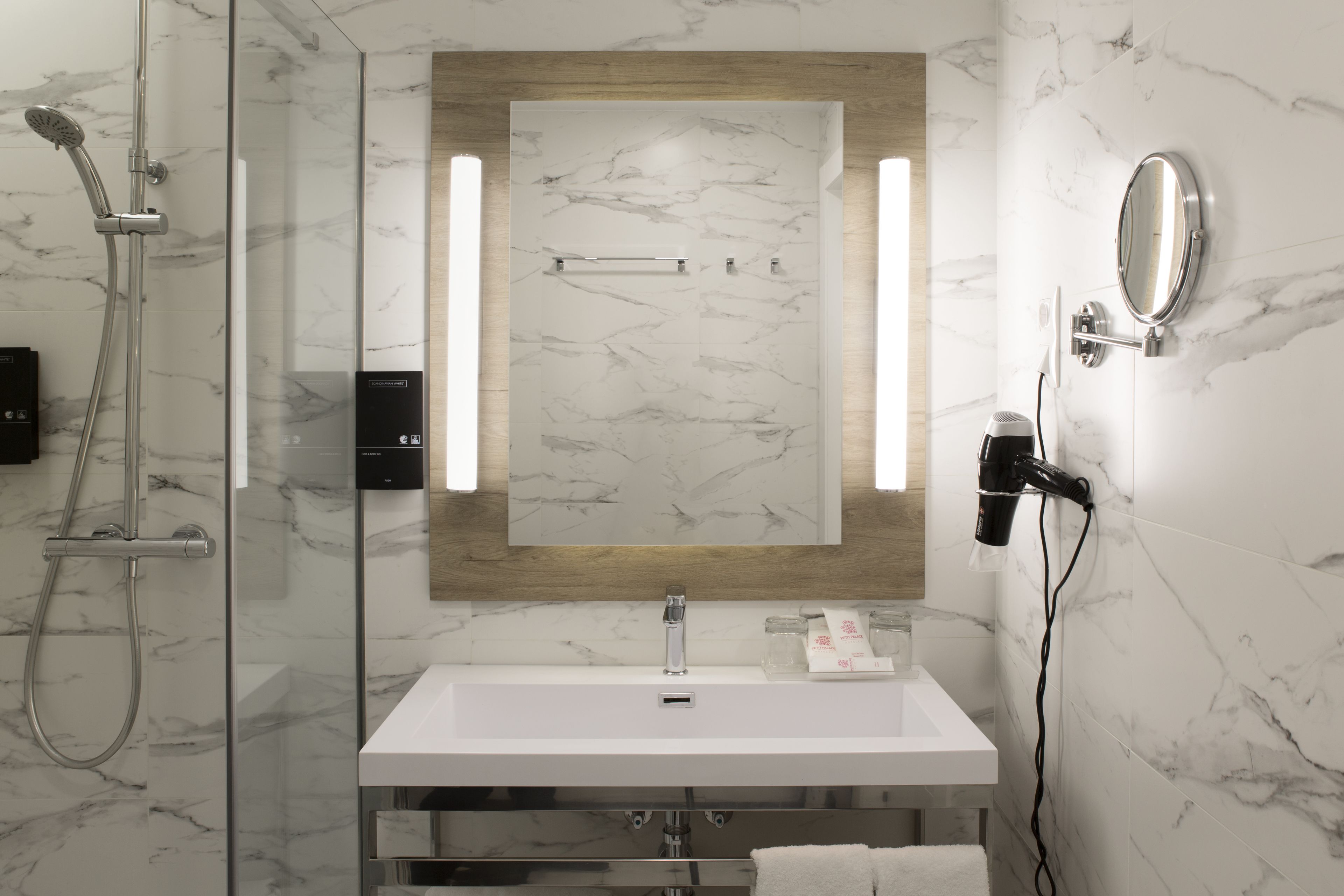 A modern bathroom with a glass-enclosed shower, a white sink, and a mirror with integrated lighting.